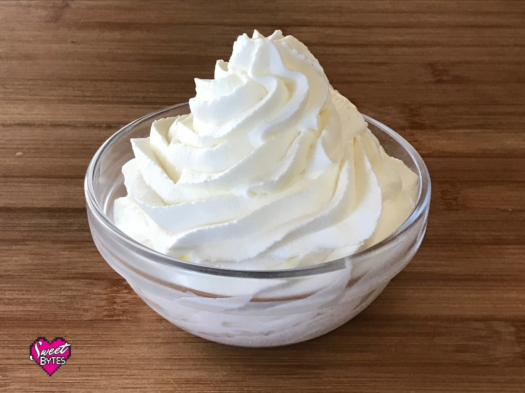 Homemade Whipped Cream A small glass bowl on a wooden table filled with a heaping swirl of homemade stabilized whipped cream