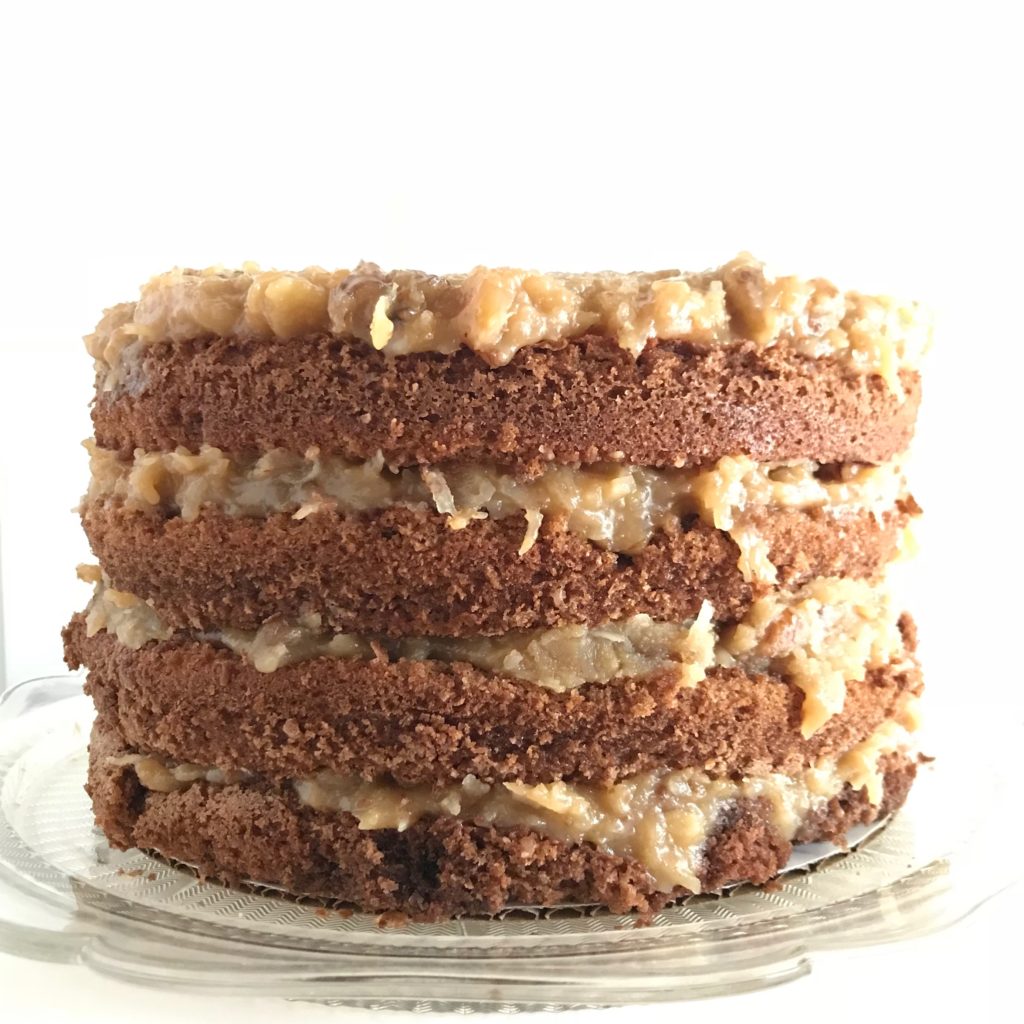 An 8", 4 layer, round german chocolate cake on a depression era clear glass cake plate.