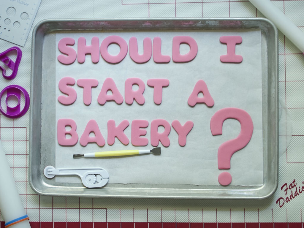 Pink letters cut out of fondant arranged on a half sheet pan covered in parchment paper with a large pink question mark. Two sugar sculpting tools are arranged on the sheet under the phrase Should I Start a Bakery