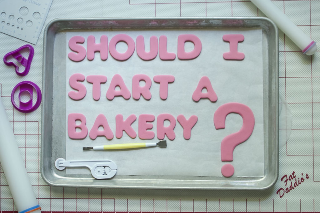Pink letters cut out of fondant arranged on a half sheet pan covered in parchment paper with a large pink question mark. Two sugar sculpting tools are arranged on the sheet under the phrase Should I Start a Bakery
