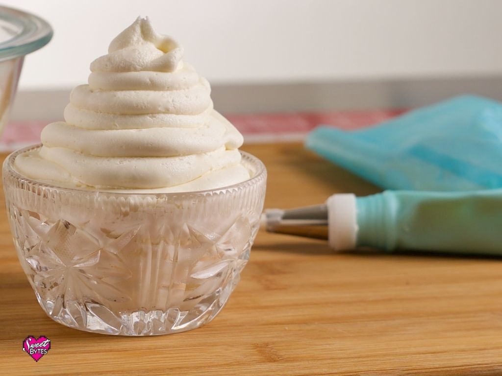 A crystal bowl filled with vanilla buttercream, a piping bag lies to the right of the bowl