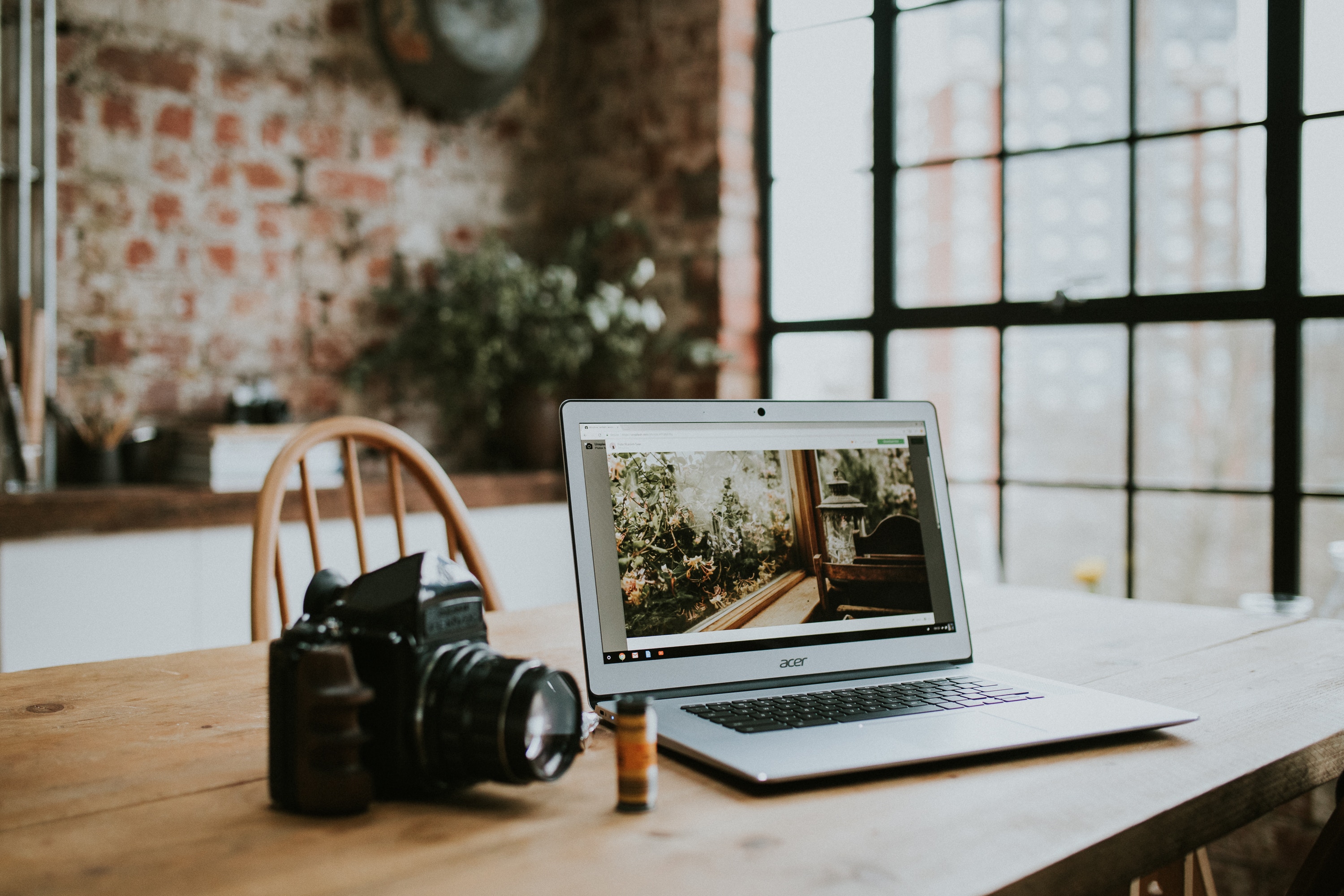 Wooden Desk with camera to the left of a laptop