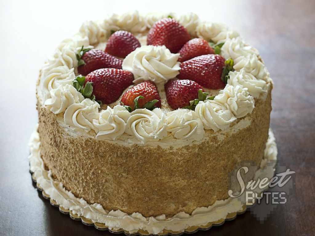 A round layer cake with white whipped cream swirls and halved strawberries on top.