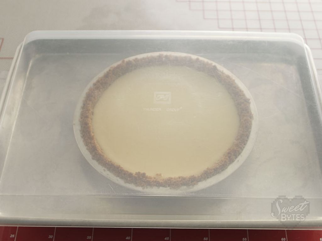 Key lime pie needs to chill in the refrigerator at least 4 hours before serving. #sweetbytesokc #pie #keylimepie A baked key lime pie on a baking sheet with a plastic lid, ready for the refrigerator