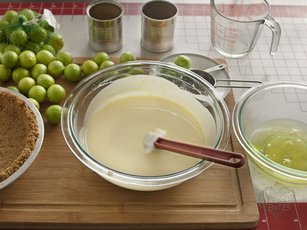 Key lime pie filling for the best key lime pie from Sweet Bytes OKC! #pie #keylimepie #sweetbytesokc #baking A glass bowl filled with key lime pie filling a red handled spatula sticks out of the bowl.
