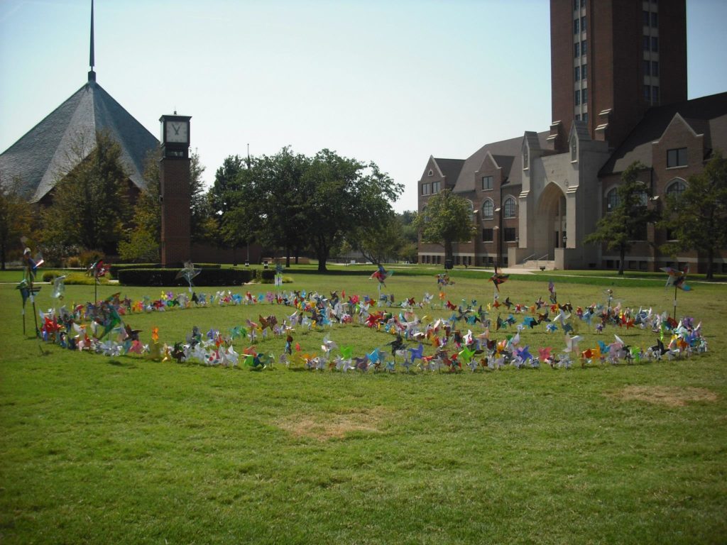 A grassy field at OCU with handmade pinwheels forming a peace sign. 