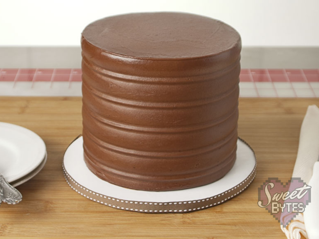 This chocolate cake recipe from scratch will be your new favorite chocolate cake. Definitely put it in your recipe box! #baking #cake #chocolatecake #sweetbytesokc #recipe #sweettreat Finished six inch, four layer chocolate cake from scratch frosted with chocolate cake frosting sitting on white cake board with brown ribbon
