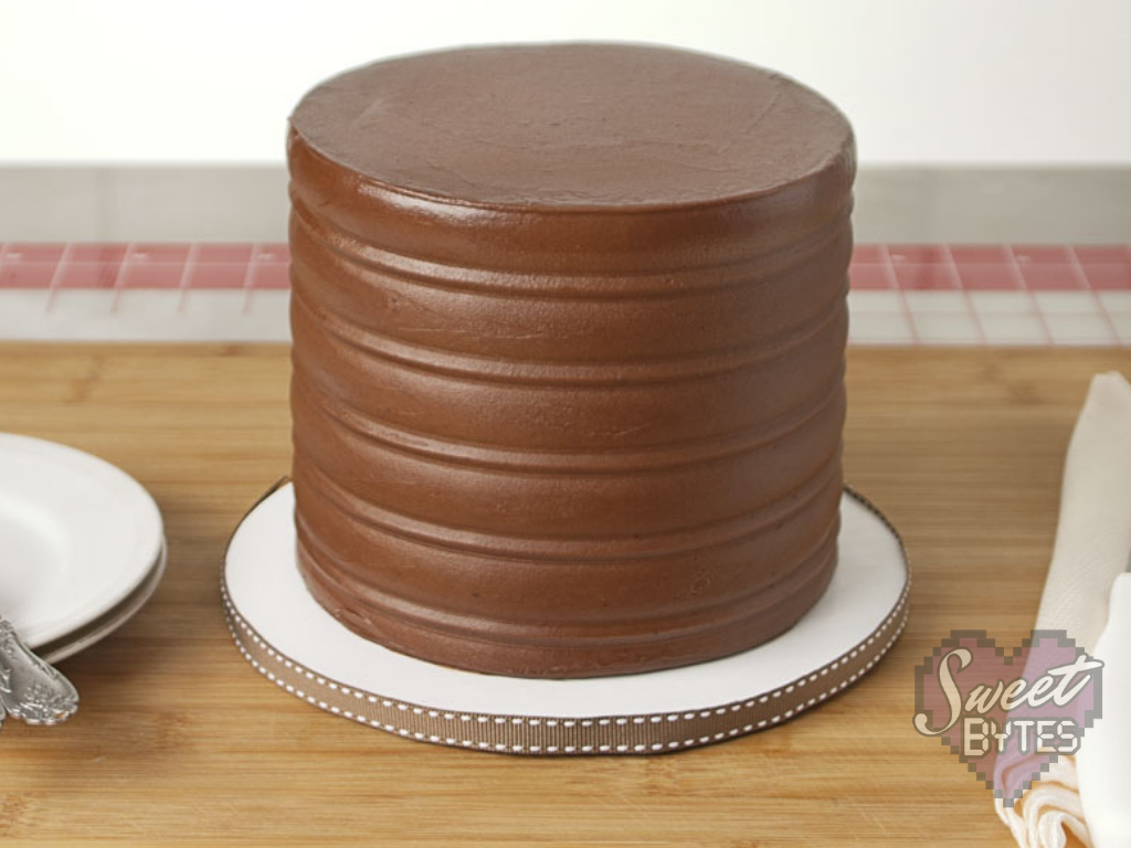 Finished six inch, four layer chocolate cake from scratch frosted with chocolate cake frosting sitting on white cake board with brown ribbon