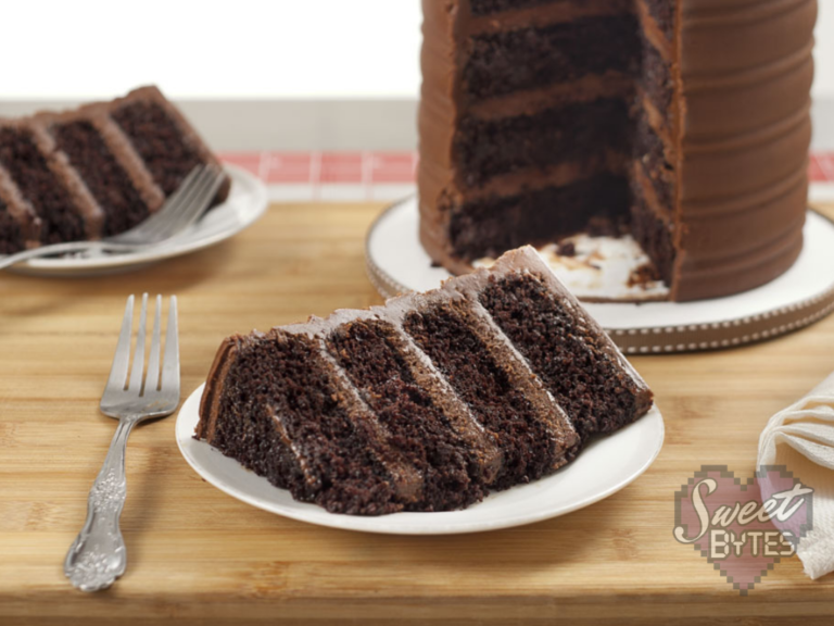 Four layer chocolate cake slice on white dessert plate with the sliced chocolate cake behind it