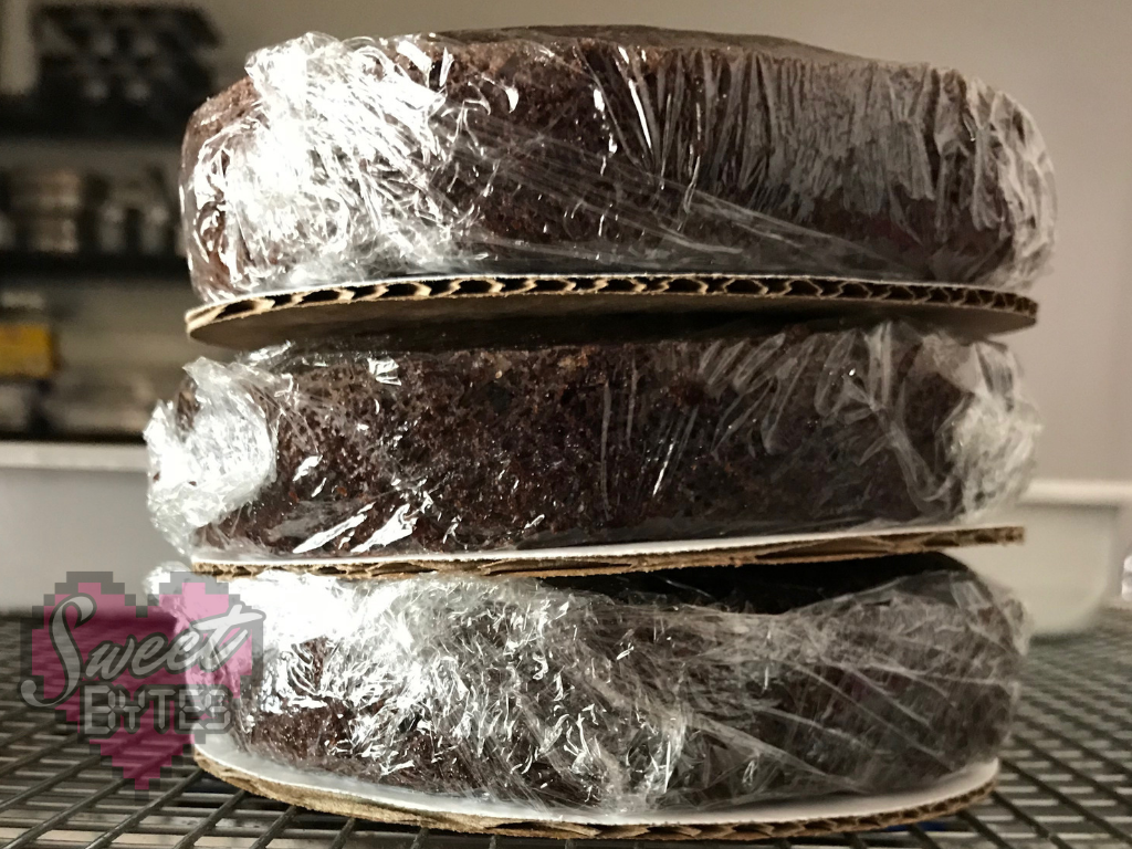 3 chocolate cakes layers wrapped in plastic to show how to store baked cake layers