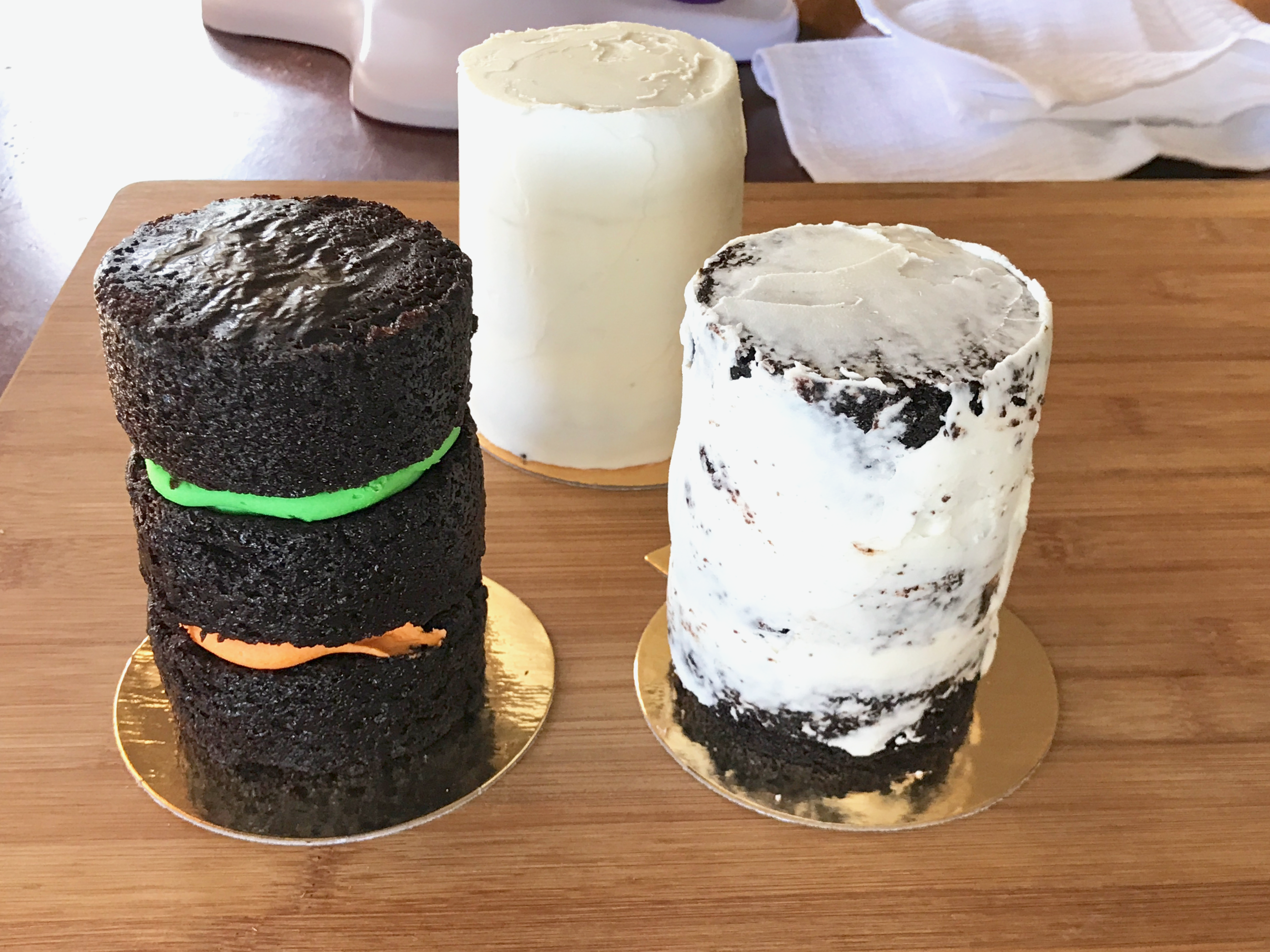 Three 3 layer mini chocolate halloween cakes each in a different state of completion. One naked, one crumb coated, one completely frosted. 
