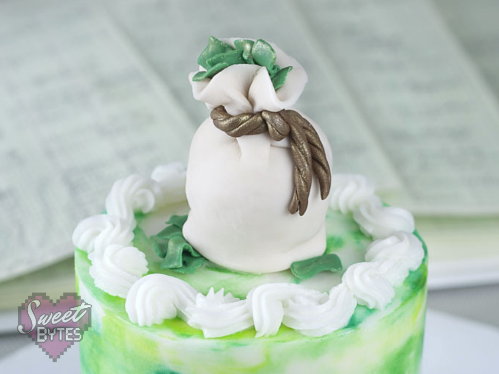 Knowing the Real Costs of Your Bakery Items is the Secret to Pricing. top of a small green and white cake with a fondant money bag cake topper with green fondant money coming out of the top and bottom for the costs of bakery items