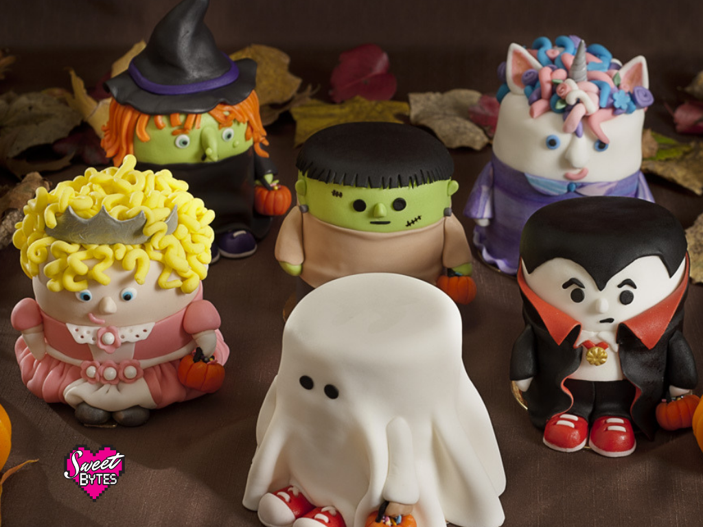 A group shot of 6 mini Halloween cakes covered in fondant. A ghost, princess, Frankenstein, Dracula, witch, and unicorn