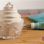 A crystal bowl filled with vanilla buttercream, a piping bag lies to the right of the bowl