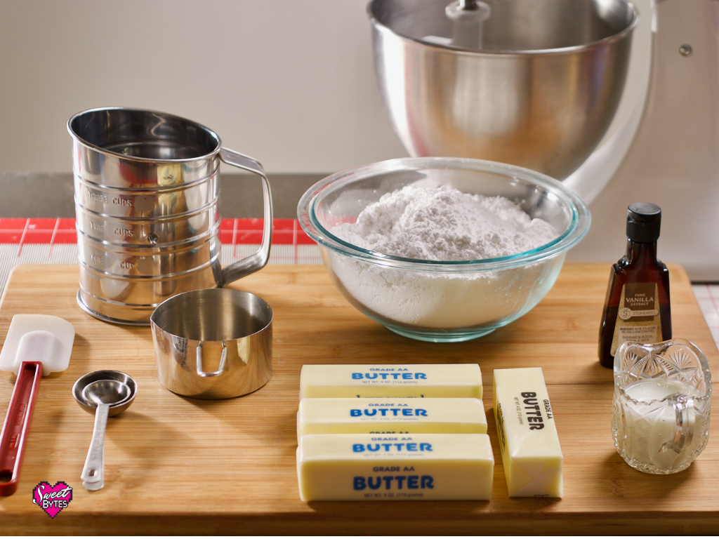 Vanilla buttercream ingredients and equipment on a maple cutting board. A white KitchenAid mixer is in the background. 