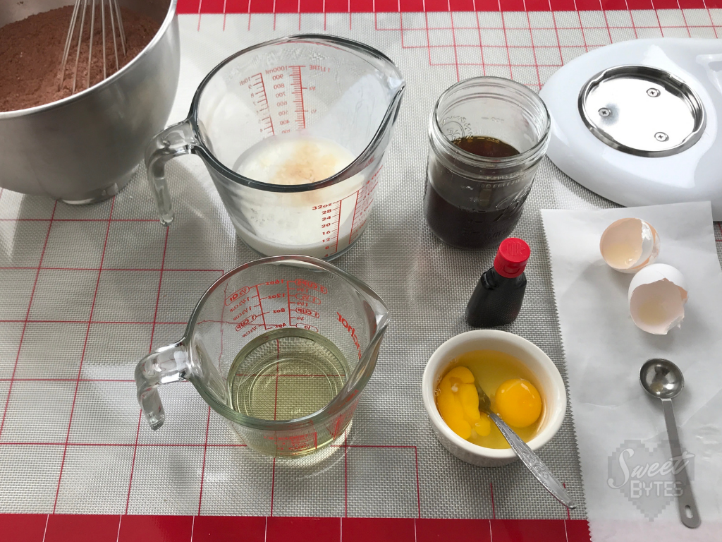 Overhead photo of measuring cups filled with wet ingredients for the chocolate cake arranged on a gridded silicon mat