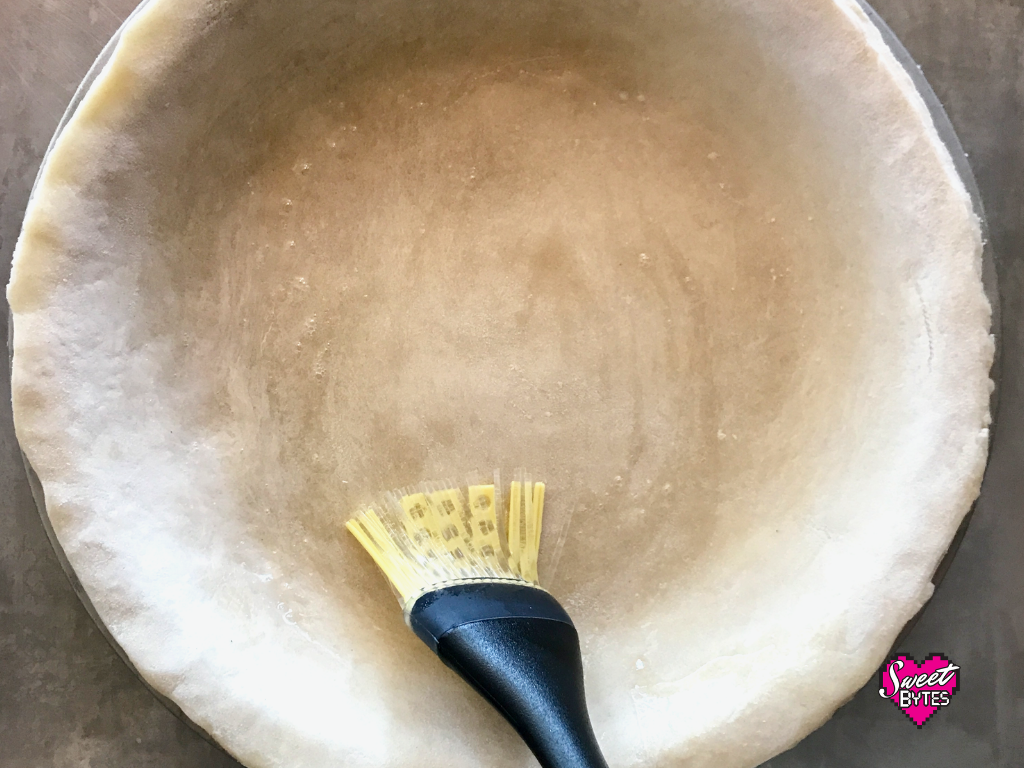 A raw pie crust being brushed with liquid egg white before baking pie crust 