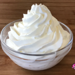 A small glass bowl filled with a heaping swirl of whipped cream