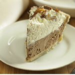 Slice of French Silk Pie with whipped cream and chocolate curls on top arranged on a white plate.