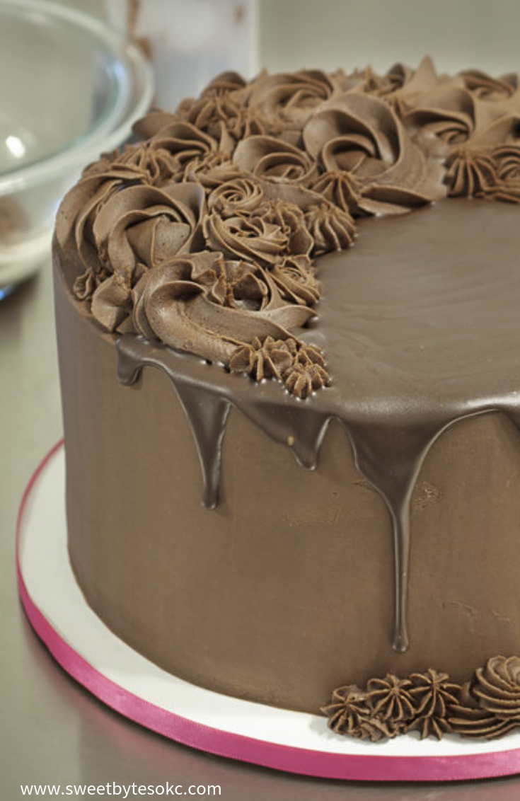 A cropped view of a ganache covered cake with piped decorations and a chocolate drip