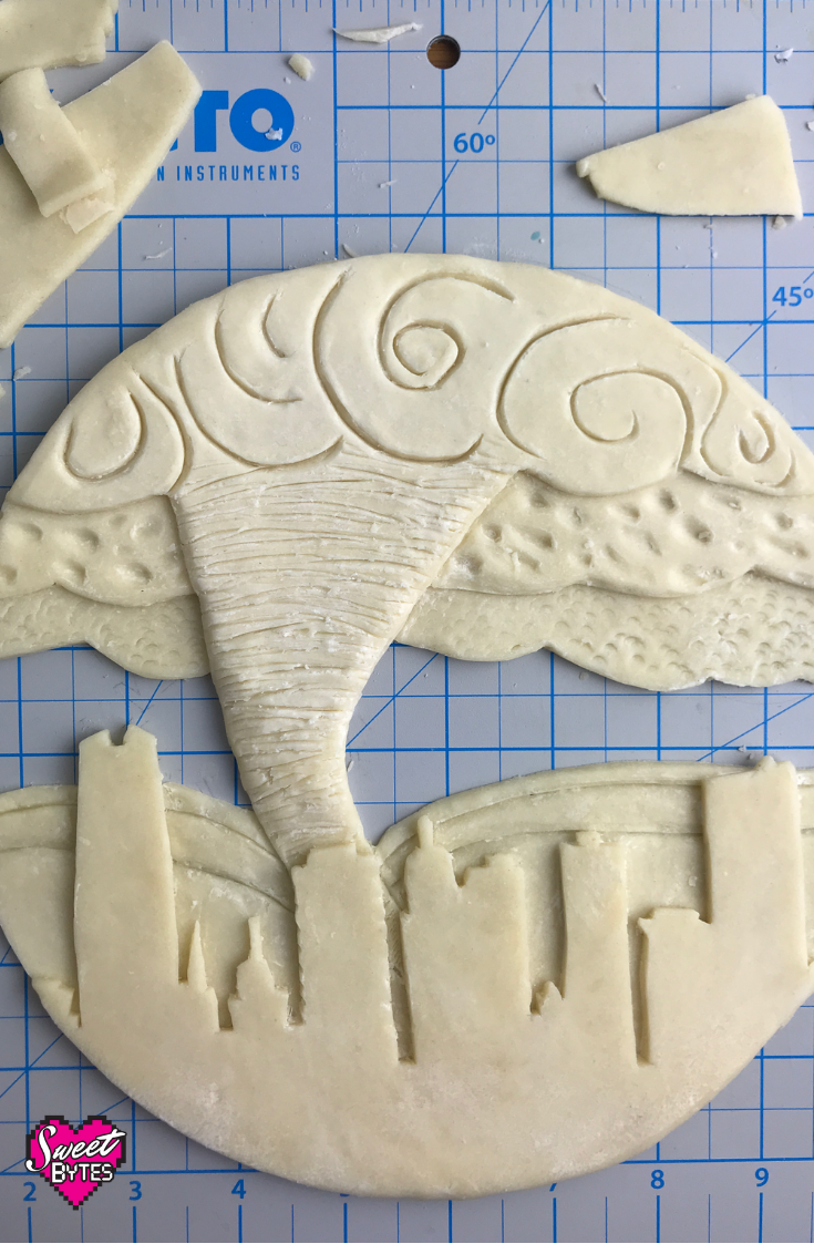 OKC Pie crust in progress on a cutting mat. Downtown OKC with a tornado behind it