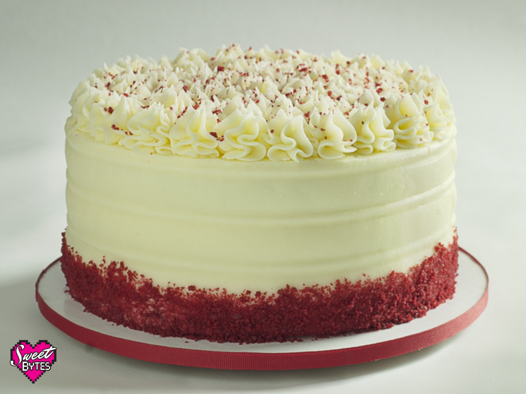 Red velvet cake with cream cheese frosting and red cake crumbs around the bottom