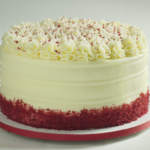Red velvet cake with cream cheese frosting and red cake crumbs around the bottom
