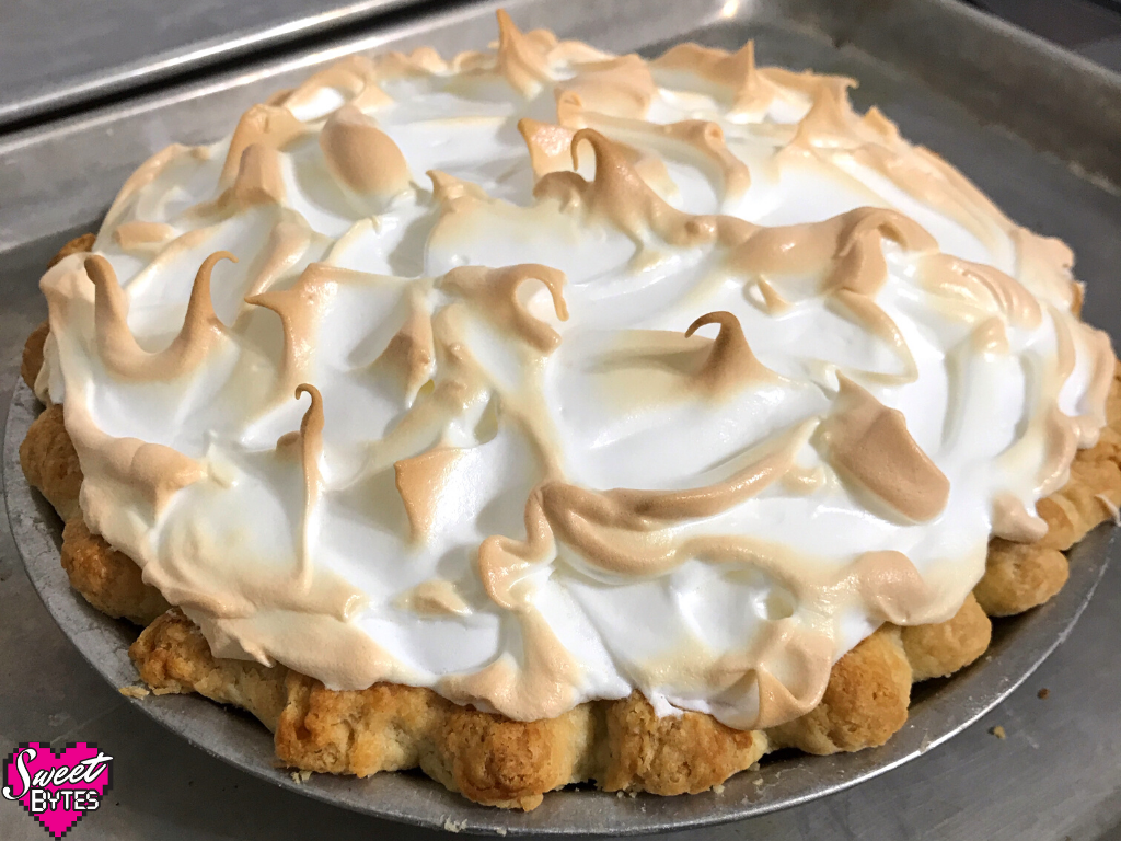 A beautiful lemon meringue pie with a toasted meringues sitting on a baking sheet