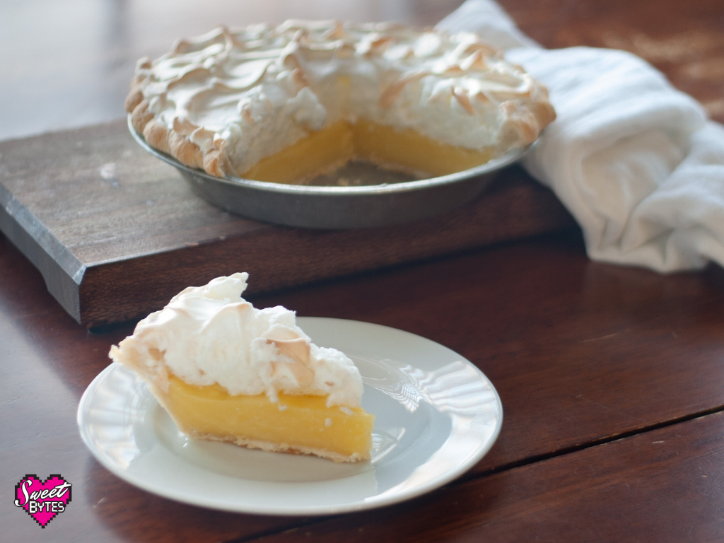 Slice of lemon meringue pie in the foreground with a whole sliced lemon meringue pie in the background for lemon meringue pie recipe