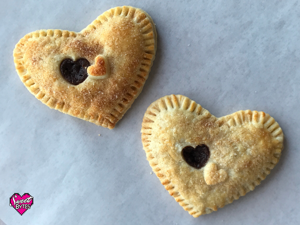 Two baked heart-shaped hand pies arranged on a white parchment paper. 