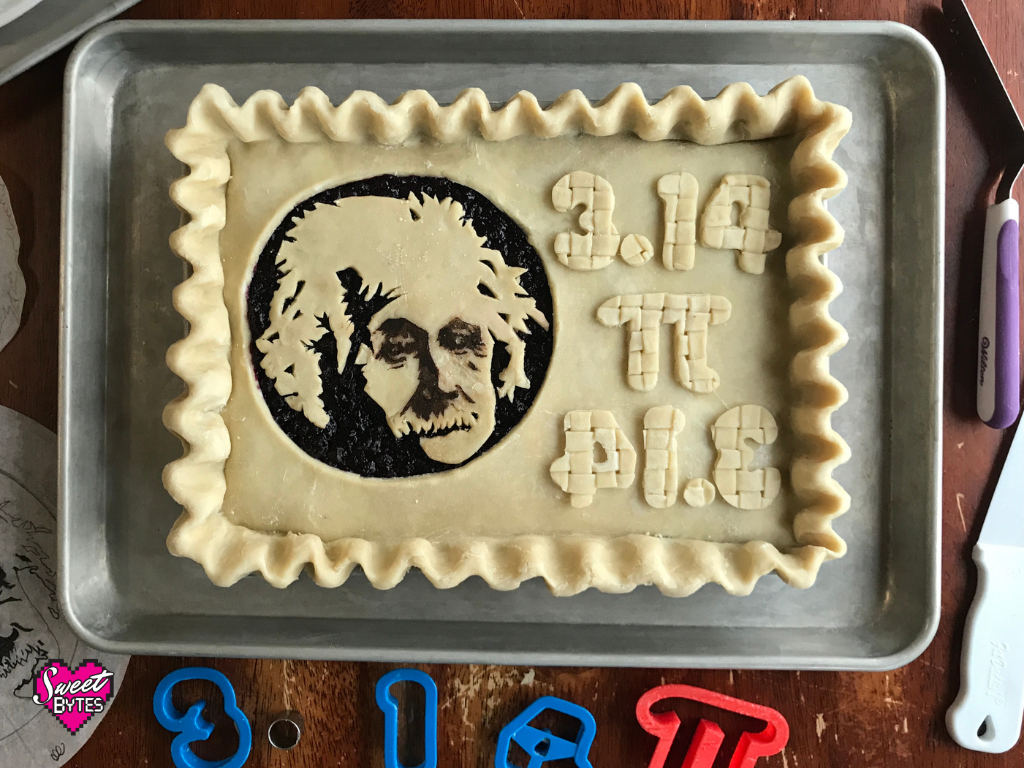 Unbaked rectangular pie with Albert Einstein's face on it. The numbers 3.14 are written in pie crust cut out numbers, then again backwards as the word pie also cut out of pie crust