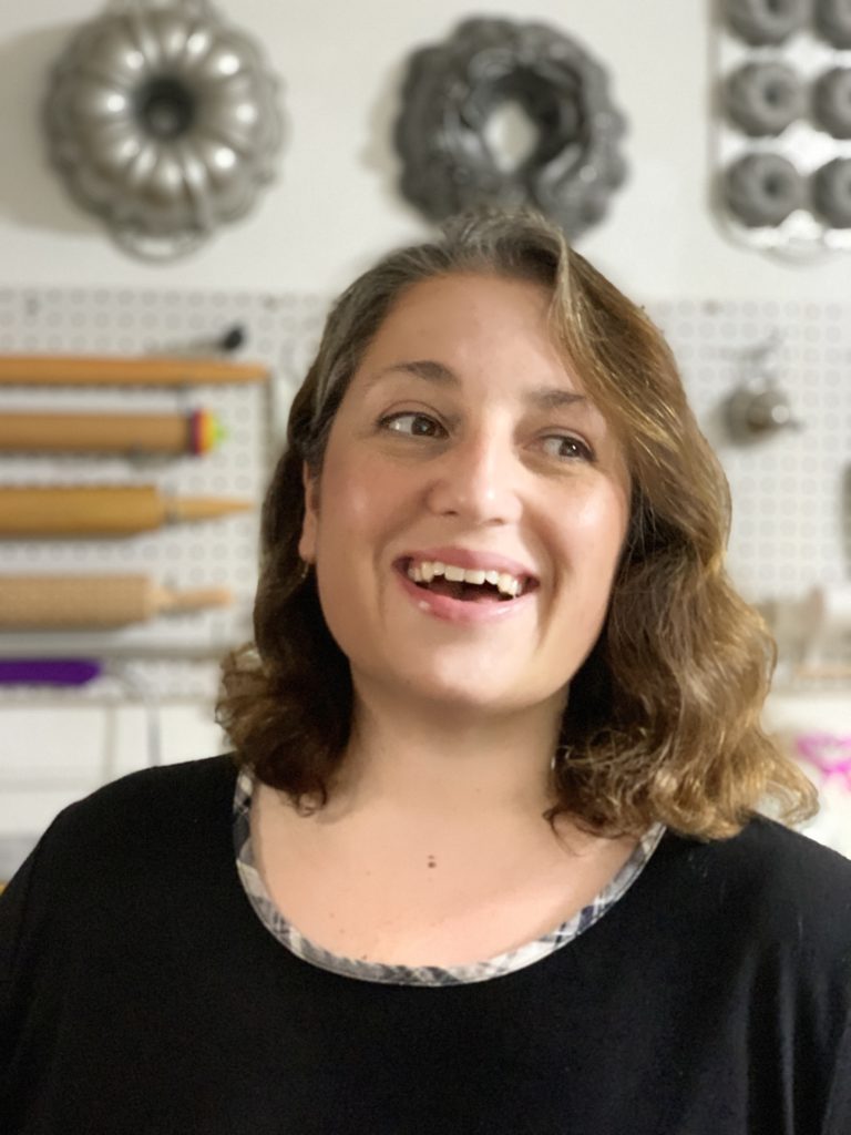 Photo of Mikel Ibarra from Sweet Bytes laughing, behind her is a pegboard wall with rolling pins and bundt cake pans.