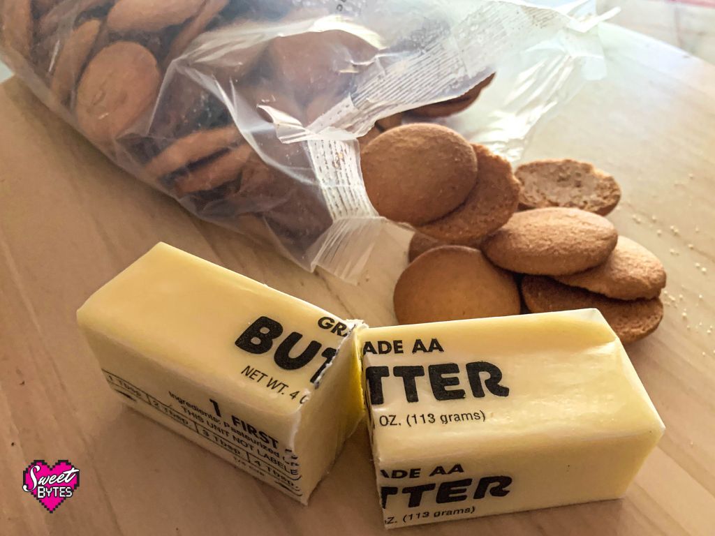 A stick of salted butter and an open package of vanilla wafers on a wooden cutting board