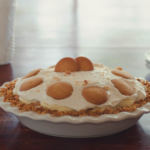 a banana pudding pie with vanilla wafer crust sitting on a table with sun coming in from the window behind the table