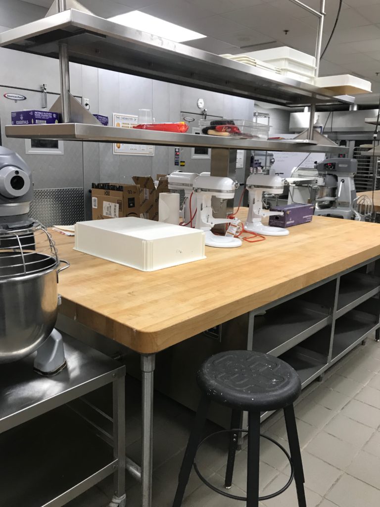 A maple topped work table with a stand mixer and stainless steel shelves with professional baking equipment at Francis Tuttle